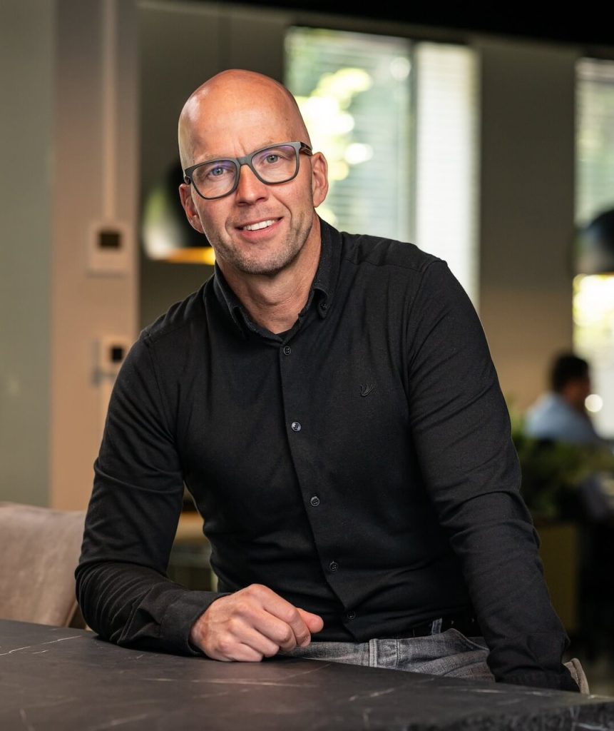 Man met bril in zwarte outfit aan tafel