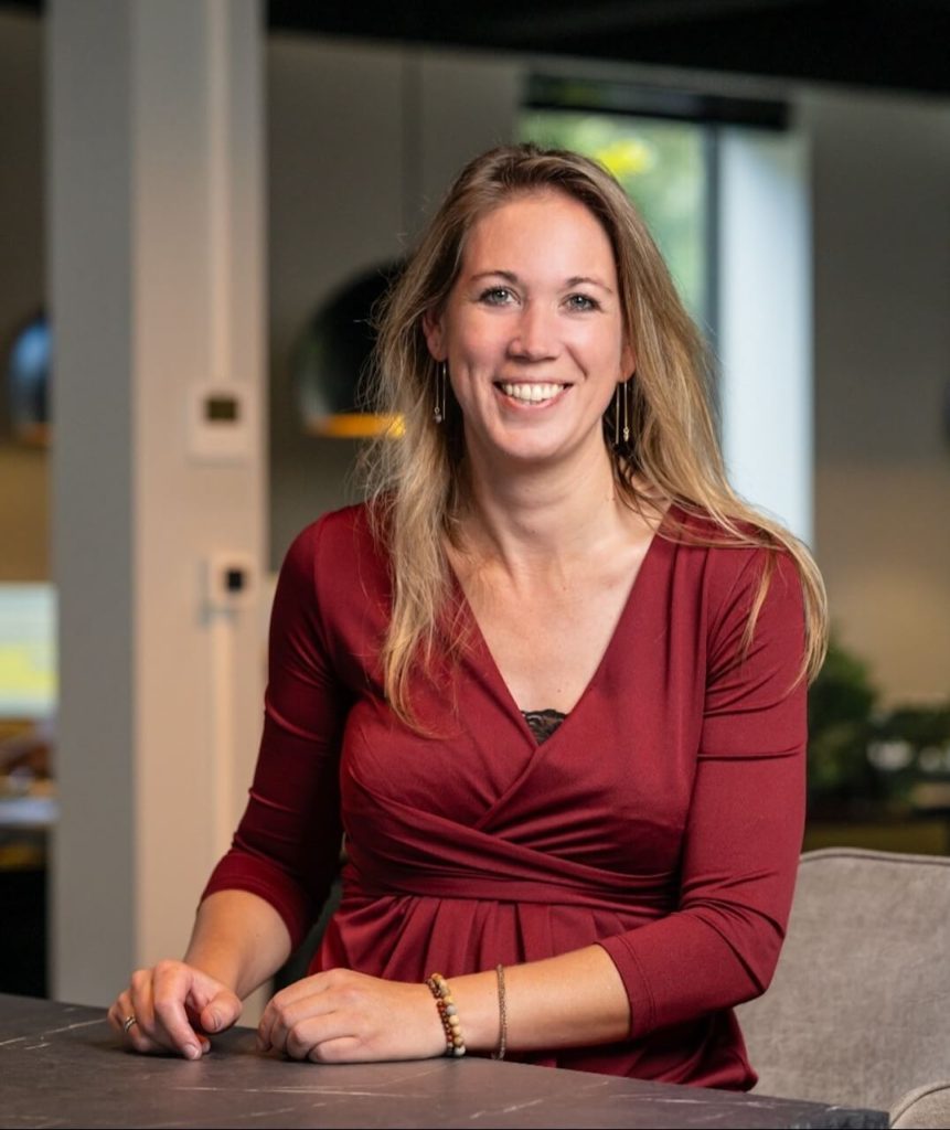 Vrouw in rode blouse glimlacht naar camera.